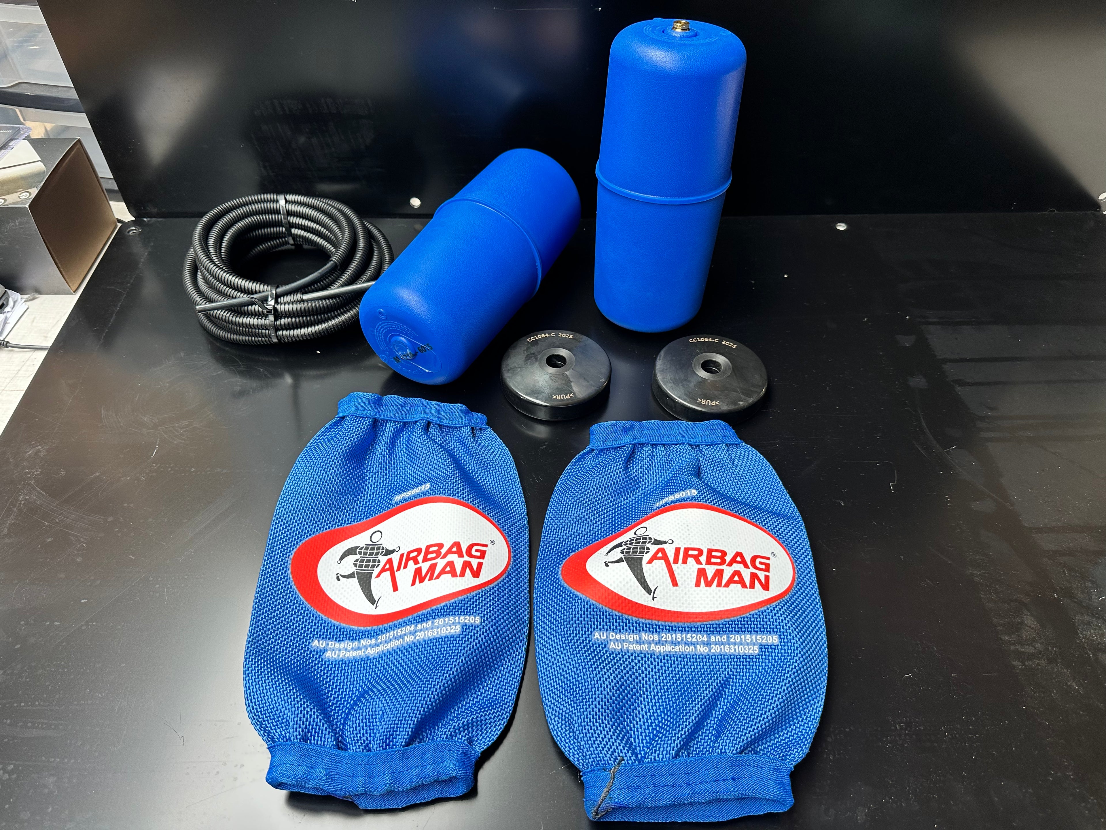 Blue airbag man products including two blue airbags, a coiled hose, and two black weights on a black surface.